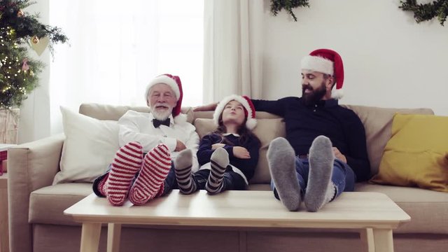 A small girl with father and grandfather sitting on a sofa at Christmas time, having fun.