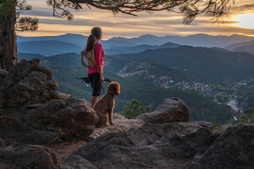 A hispanic woman is hiking with a dog, at sunset, in the Rocky Mountains near Denver, Colorado, USA