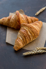 Breakfast. Croissants with wheat ears at baking paper on dark background