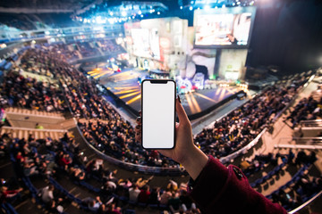 Close up of a woman holding smartphone with blank screen mobile with concert blurred background.