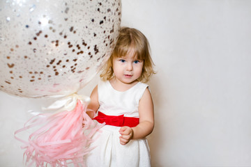 Little blonde baby girl two years old with big pink and white balloons on her birthday party