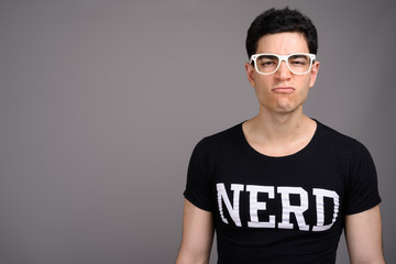 Young handsome nerd man with eyeglasses against gray background