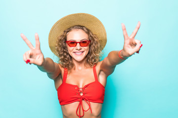 Portrait of amazing young woman showing peace gesture in red bikini isolated over green background.