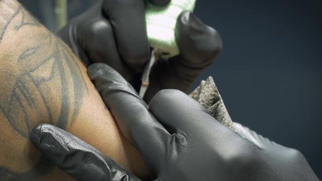Extreme closeup of a tattoo artist using a needle to ink a client in 4k. Tattoo machine punctures the skin inking a stylish design. Authentic shot represents alternative lifestyles & body modification