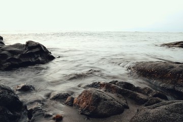 long exposure seascape of the pacific ocean from the shore with rocks and volcanic black sand
