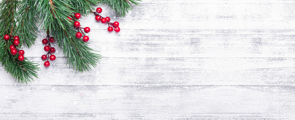 Christmas background with tree branches and holly berries. White wooden table. Snowfall drawing effect. Top view. Copy space