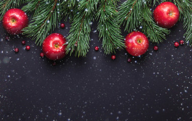 Christmas background with tree branches, red apples and cranberries. Dark wooden table. Snowfall...