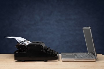 Old typewriter and laptop on wooden table