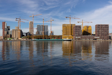 Panoramic view of urban development site with modern buildings inhabited by cranes in the Dutch city of Rotterdam reflected in the water