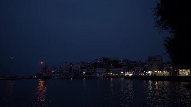 View of the city pier from the sea at night. Reflection of light in water. 4K
