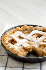Home-baked apple pie on cloth over white wooden background, side view. Copy space.