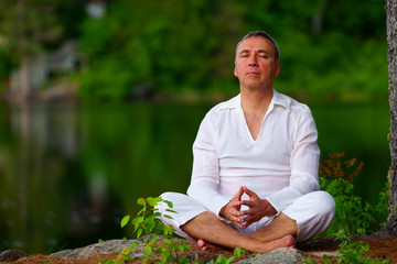 Naklejka na ściany i meble Portrait of a proud healthy caucasian man, 50, wearing a white suit, after a meditation session by the river at the sunset.