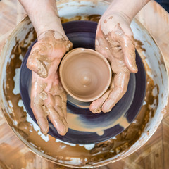 Pottering Ideas. Closeup of Dirty Male Potter Hands Moulding Jar on Potter's Wheel in Workshop.