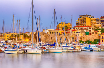 Panorama of Old Venetian Harbour with Lines of Ships and Fishing Boats At Blue Hour in Heraklion City in Greece. Slight Blurred Motion of The Boats Due to Wind and Sea Waves On Foreground