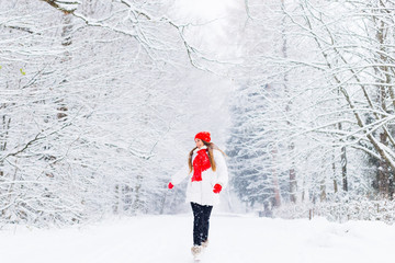 a girl with long hair in winter clothes walks in a winter park and have fun among the snow-covered trees