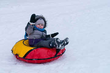 Fototapeta na wymiar cheerful child boy in winter on a sled against a white snow