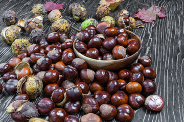 pile of aesculus hippocastanum or conker tree nuts and autumn leaves on wooden table