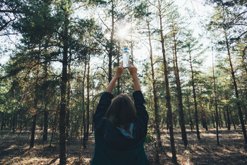 Young blond attractive girl holds tightly with hands a plastic bottle with water in the forest. Clear fresh water from the lake. Concept of the danger of pollution of the wild nature of plastic waste