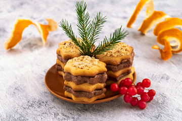 Obraz na płótnie Canvas Beautiful dessert for the holiday-cookies with chocolate layers, a branch of green spruce, red berries of viburnum, curly cut orange peel.
