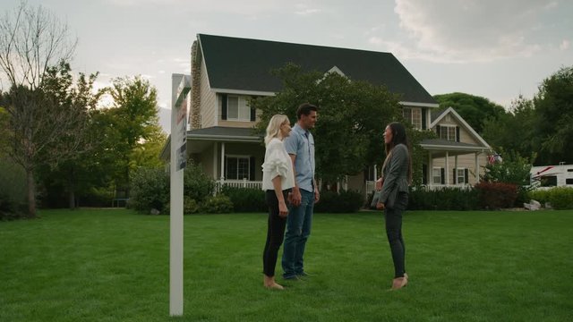 Slow Motion Panning Shot Of Realtor Shaking Hands With Couple On Lawn Of House For Sale / Pleasant Grove, Utah, United States