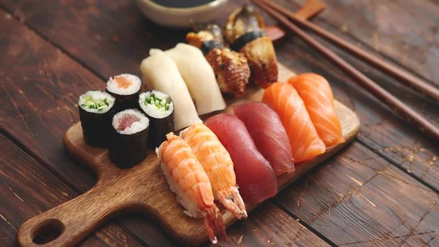 Sushi Set. Different kinds of sushi rolls on wooden serving board with soy sauce and chopsticks over dark wooden texture background. Top view with copy space.