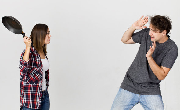 Woman with cooking pan being angry at her man. Couple standing against white background