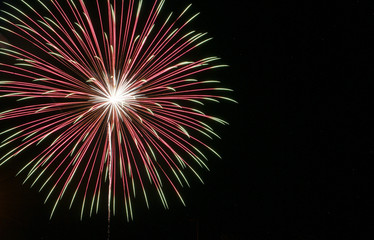 Fototapeta na wymiar Single large starburst firework with white center transitioning to red then to green in the black sky on the Fourth of July