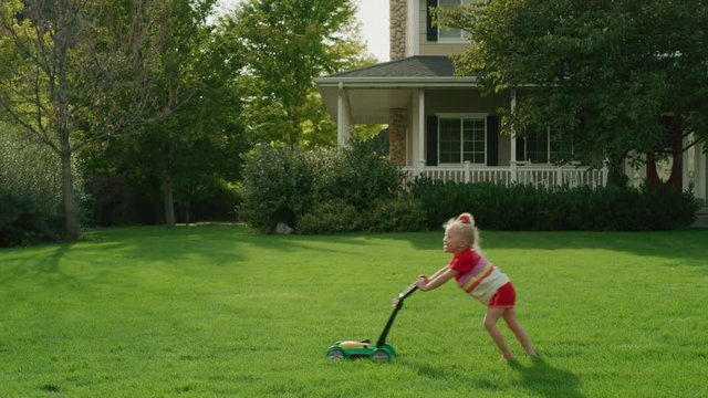 Daughter pushing toy lawnmower following father mowing lawn / Pleasant Grove, Utah, United States