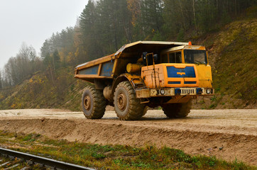 Fototapeta premium Earth mover loading dumper truck with sand in quarry. Excavator loading sand into dumper truck.Quarry for the extraction of minerals. Large quarry dump truck. Production useful minerals.