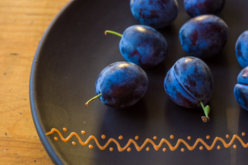 juicy blue plums in ceramic plate on wooden background