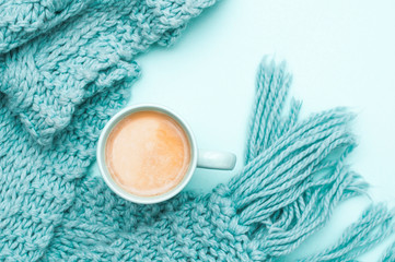 Obraz na płótnie Canvas A cup of coffee with cream and a warm scarf. Turquoise colour. Top view