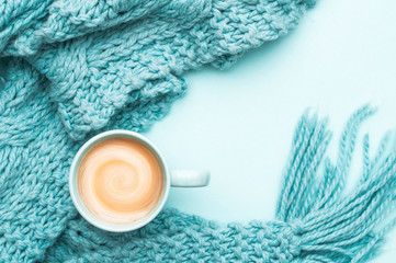 Obraz na płótnie Canvas A cup of coffee with cream and a warm knitted scarf. Turquoise colour. Top view