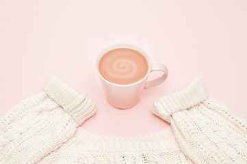 A cup of aromatic coffee with cream and a warm sweater on a pink background