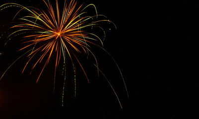 Green, gold, and red trailing light of firework against a black sky on the fourth of July