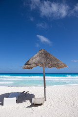 Sun umbrella with wooden lounge chairs on tropical shore