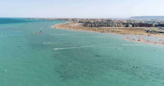 Wide aerial, people parasail near tropical city