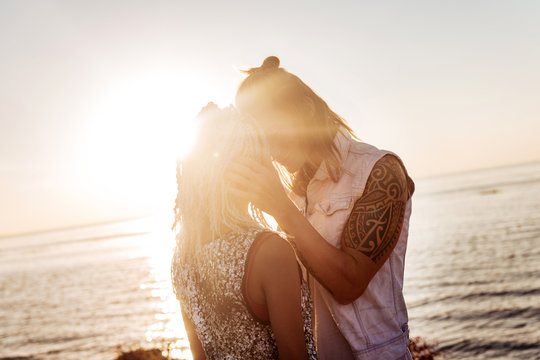 Kissing girlfriend. Caring loving handsome man with tattoo kissing his girlfriend with dreadlocks