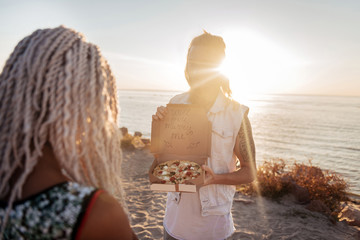 Cute boyfriend. Cute boyfriend opening box with pizza asking his woman to marry him standing near the sea