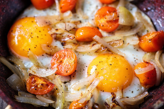 Background of Fried eggs in a frying pan with cherry tomatoes and onion