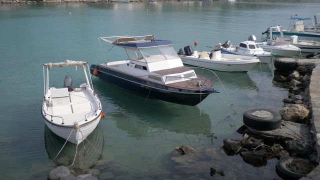 Small fiberglass rowboats stay along pier, Ted to boys and land. Many simple vessels moorage along embankment road. Calm weather. The pier of the island of Crete. 4K
