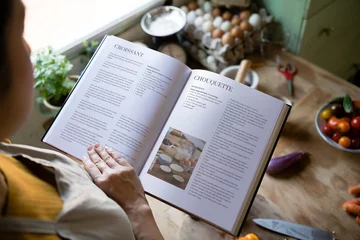 Badkamer foto achterwand Happy woman reading a cookbook in the kitchen © Rawpixel.com