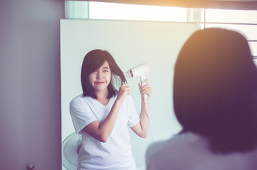 Beautiful asian woman drying  hair at front of mirror,Female drying her short hair with dryer
