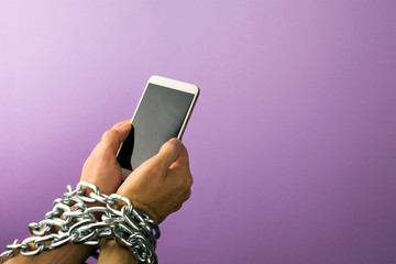 hands tied with metallic chain to smartphone. concept is dependent on technology, phone, social networks