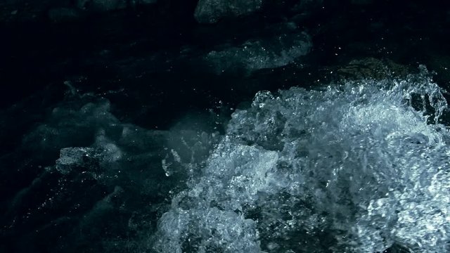 Slow motion of waves on dark water surface with play of flecks of bright light close up. Amazing dramatic natural background. Shooting with 180fps. Epic mystical and magic night view. Crystal clear