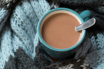 A mug of hot chocolate wrapped in a blue,gray and black scarf.