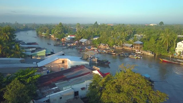 AERIAL: Flying around a bustling floating market in the sunny Vietnamese countryside. Local Asian people buying and selling produce from one wooden boat to another. Cool market on the tranquil river.