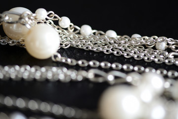 Necklace of white beads and metal chain on a dark background close up