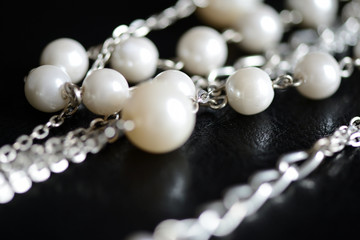 Necklace of white beads and metal chain on a dark background close up
