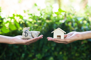  Hand holding home model change to money with green nature as background.