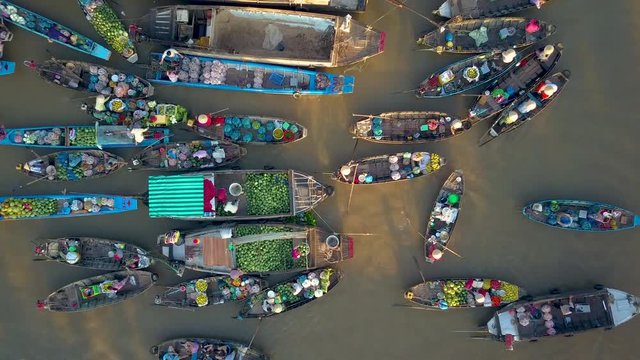 AERIAL, TOP DOWN: Local people buying and selling colorful produce from traditional wooden boats floating around the murky delta in the scenic Asian countryside on an idyllic sunny summer evening.
